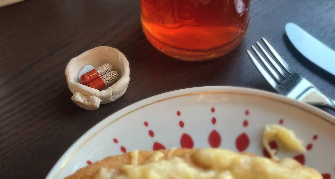 Enzymkapseln (Pankreatin) in einem kleinen Tonschälchen neben einem Teller mit Essen – unverzichtbar zu jeder Mahlzeit bei Mukoviszidose